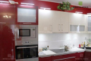 Кухня с фасадами из красного глянцевого акрила и навесными шкафчиками из белого пластика.