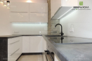 Современная п-образная кухня белого цвета. Под навесными шкафчиками встроена светодиодная подсветка.